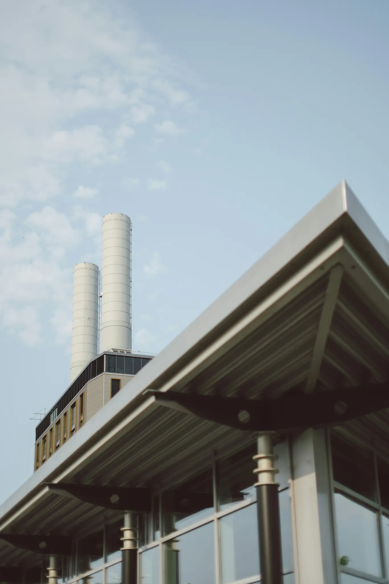 A low-angle shot of a modern building with a large, ribbed metal overhang in the foreground, and two tall, white industrial…
