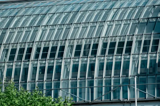 A close-up of a modern building's glass facade, featuring a curved roof and multiple rectangular windows.