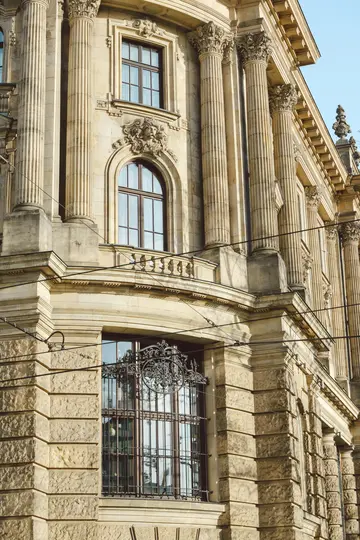 A close-up, upward-angled view of a classical building's stone facade, featuring fluted columns, arched windows, and…