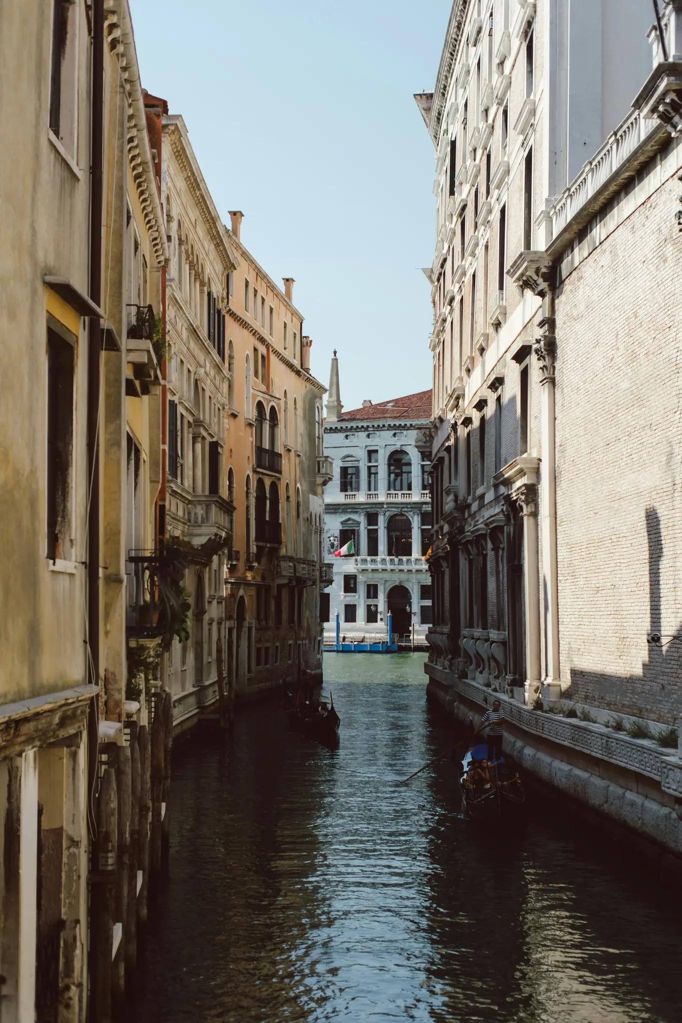 En smal kanal i Venedig, Italien, med høje, gamle bygninger på begge sider. To gondoler på det mørke vand.