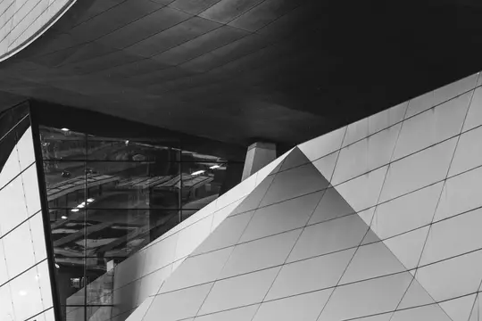 Et sort-hvidt billede af en moderne bygnings facade med skarpe vinkler, reflekterende glas og geometriske paneler.
