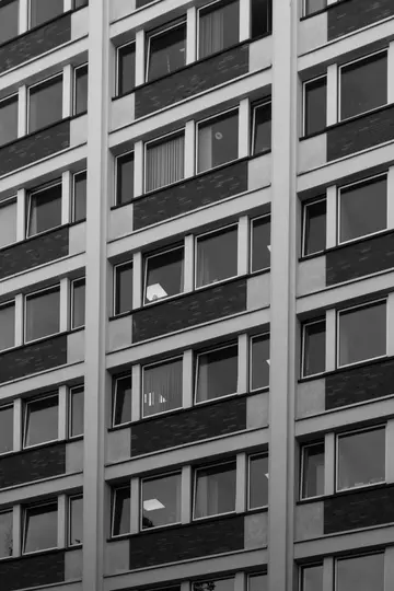 Et sort-hvidt, nærbillede, lodret billede af en bygningsfacade med mange rektangulære vinduer og murstenssektioner.