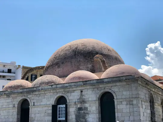 A large, weathered, pinkish-brown dome dominates the center, surrounded by smaller domes and stone walls with arched windows.
