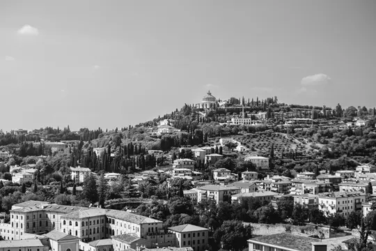 A black and white wide landscape photo of a city built on a large hill, featuring a prominent domed building at its peak.