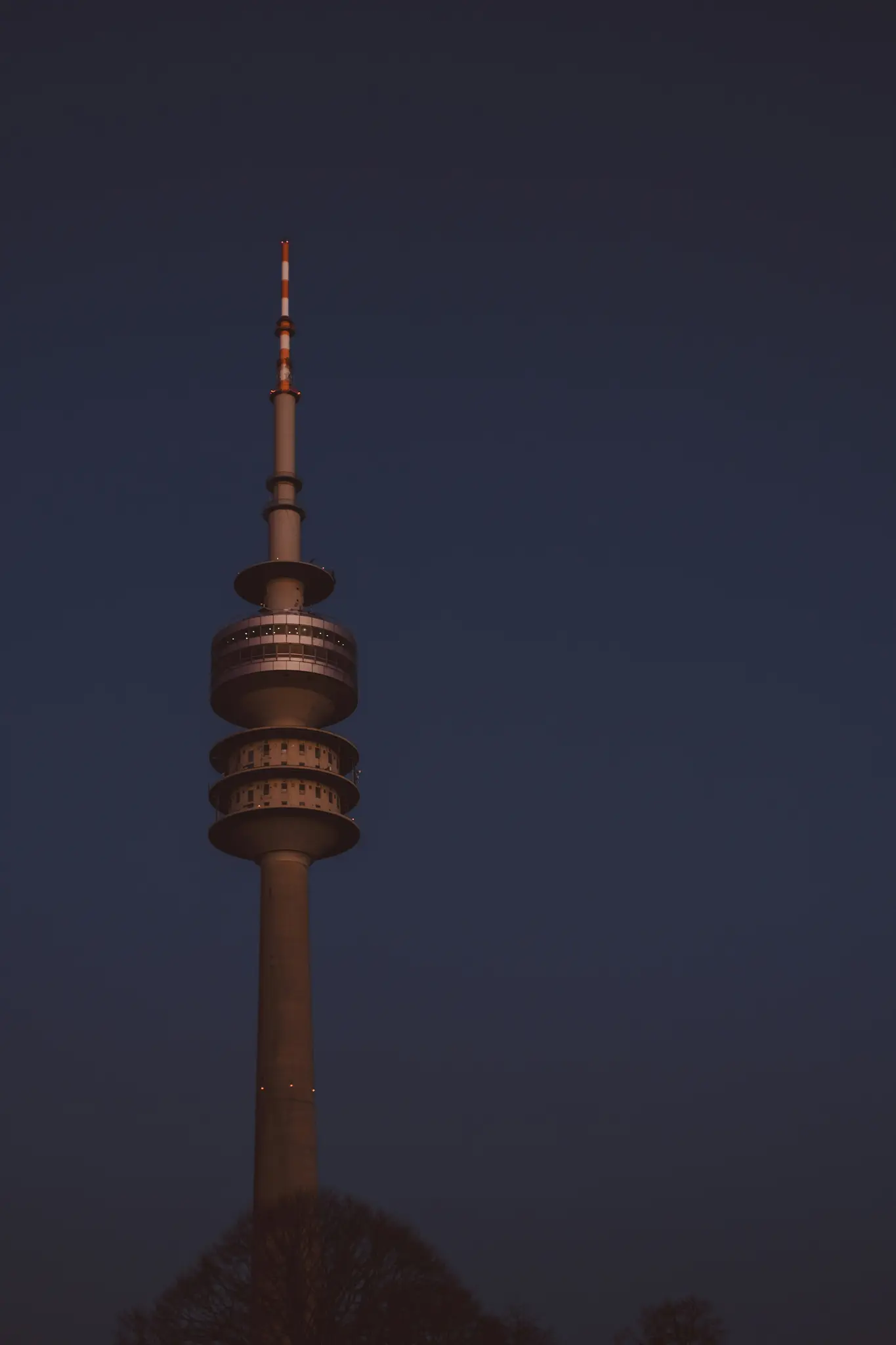 Ein hoher, grauer Telekommunikationsturm mit mehreren Aussichtsplattformen und einer gestreiften Antenne vor einem
