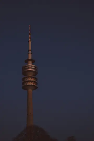 A tall, grey telecommunications tower with multiple observation decks and a striped antenna against a dark blue evening…