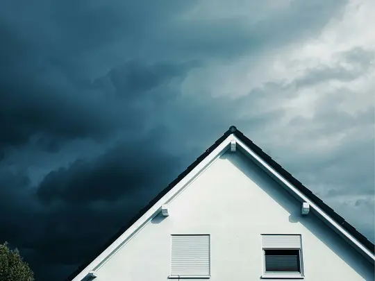 A stark image of a white house's gable and dark roofline against a sky filled with dark, heavy storm clouds.