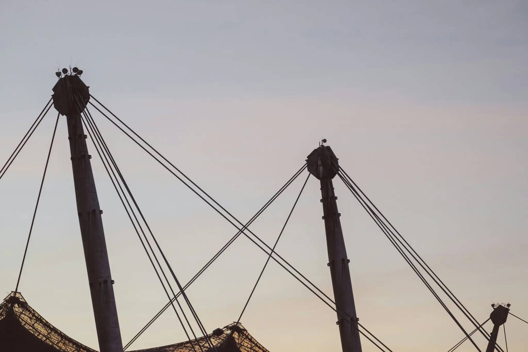 Two large concrete pillars with multiple tension cables extending from their tops are silhouetted against a pale, overcast…