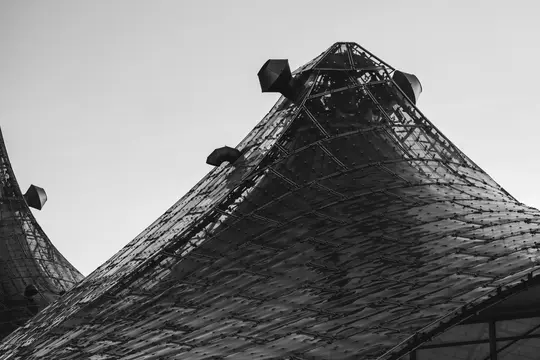 A low-angle, black and white photo of two large, dark, textured conical structures with small vents against a light sky.