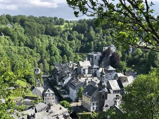Μια υπερυψωμένη θέα ενός χωριού με κτίρια με γκρίζες στέγες φωλιασμένο σε μια πράσινη κοιλάδα, περιτριγυρισμένο από πυκνά