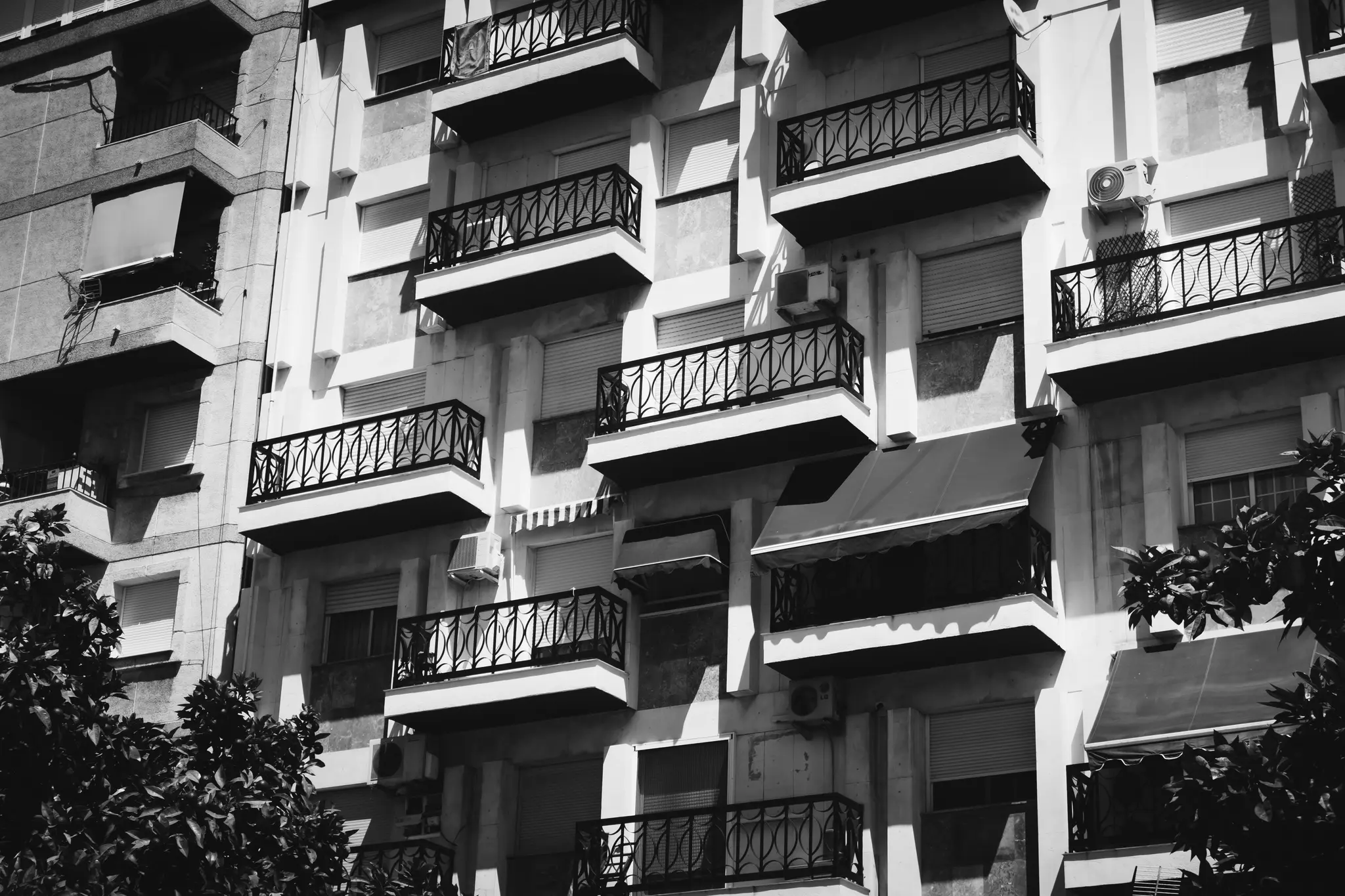 Černobílá fotografie fasády bytového domu s mnoha balkony zdobenými zábradlím a zavřenými…