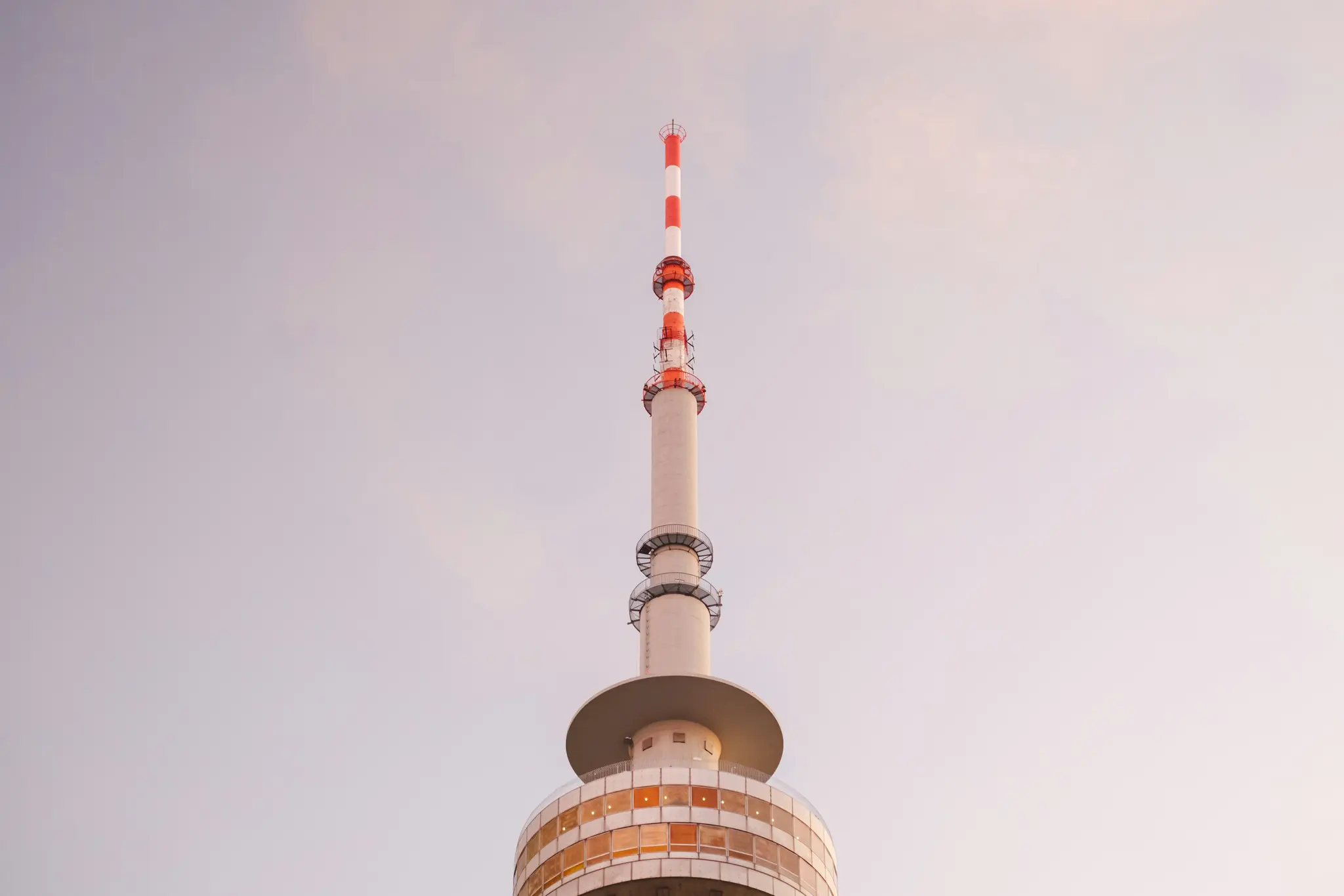 Et højt, moderne kommunikationstårn med en rød og hvid stribet antenne, en grå skakt og en cirkulær observationsplatform…