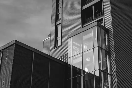 A low-angle, black and white photo of modern building facades, featuring corrugated metal, a textured wall, and a glass…