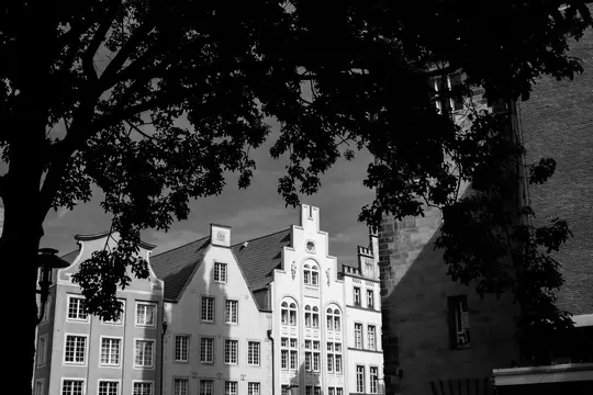 A black and white photo shows several historic buildings with ornate gables and many windows, partially hidden by a dark…