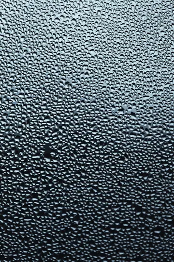A close-up, abstract photo of numerous small, irregular water droplets covering a dark, reflective surface.