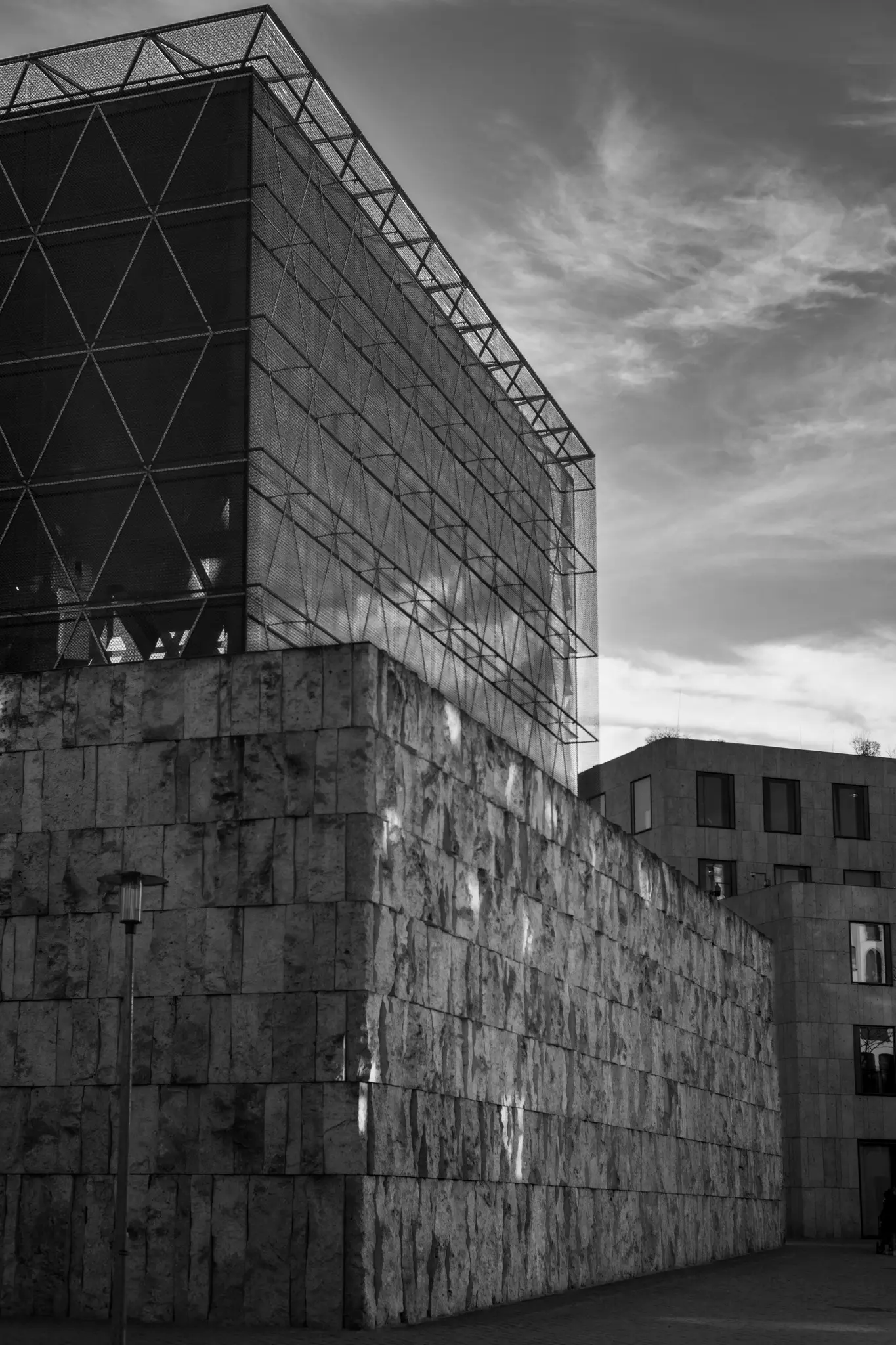 A black and white photo of a modern building with a rough-hewn stone block base and a glass and metal upper section.
