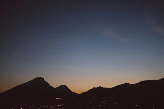 Et bredt landskabsfoto, der viser mørke bjerg silhuetter mod en gradient tusmørkehimmel fra dyb blå til orange.