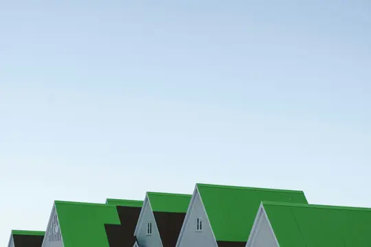 A low-angle shot of several houses with bright green corrugated roofs and light grey gables against a clear blue sky.