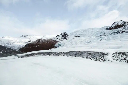 A vast, snow-covered glacier stretches across the frame, with rugged, dark mountains rising in the background.