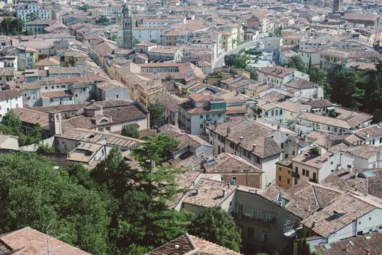 An expansive aerial view of a European city, showing a dense cluster of buildings with terracotta tiled roofs under an…