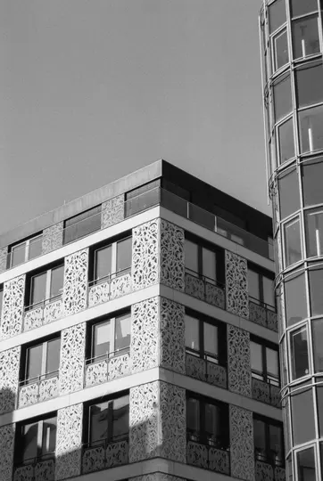 A black and white photo of two modern buildings. One has a flat facade with intricate, swirling patterns. The other is…