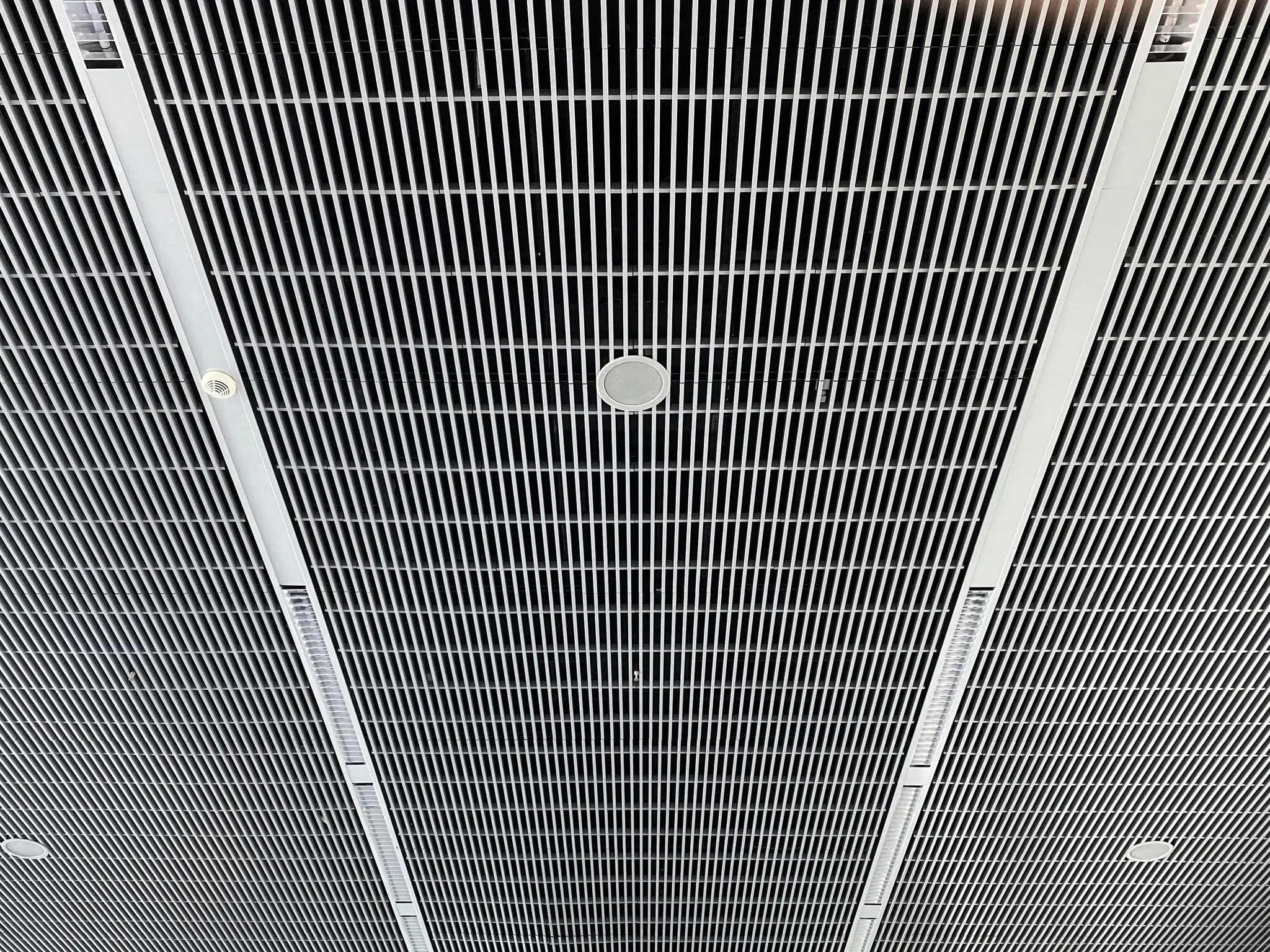 A low-angle view of a modern ceiling featuring a grid of thin white vertical slats against a dark background. Integrated…