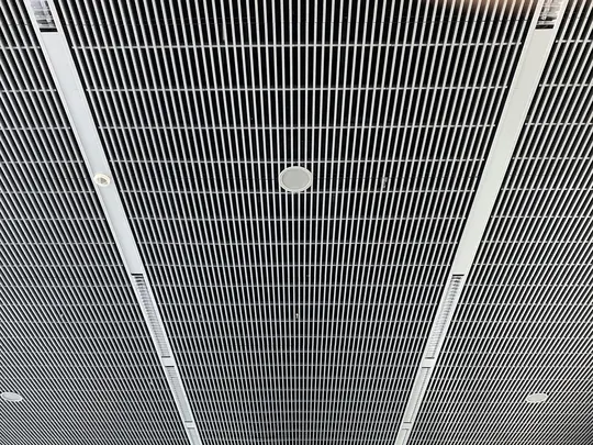 A low-angle view of a modern ceiling featuring a grid of thin white vertical slats against a dark background. Integrated…