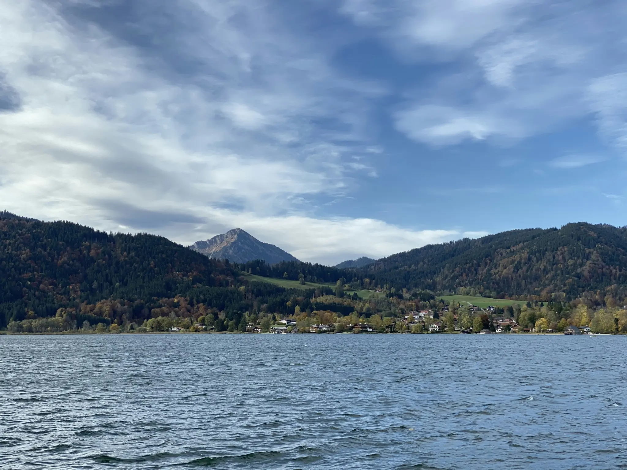 Breite Landschaftsaufnahme eines Sees mit Wellen auf der Oberfläche, der einen teilweise bewölkten Himmel widerspiegelt. Am
