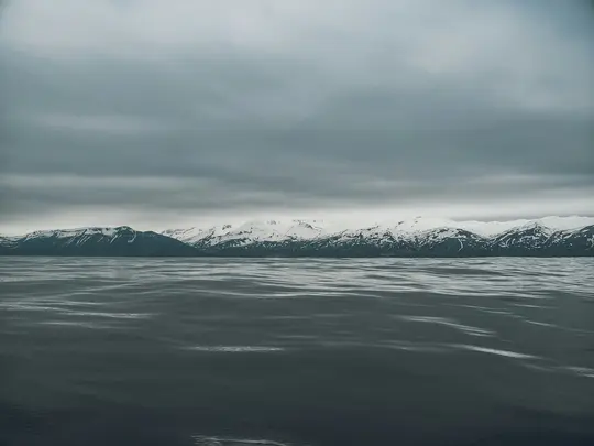 En vid bild av mörkt, krusande vatten i förgrunden, med en lång rad snöklädda berg i mellangrunden.