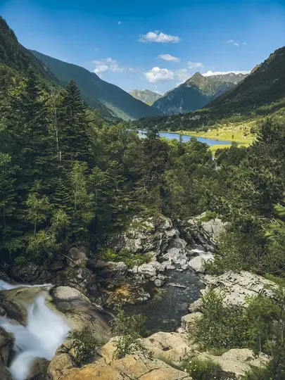 Ett levande berglandskap med en forsande flod i förgrunden, som flyter ut i en klar sjö belägen mellan gröna…