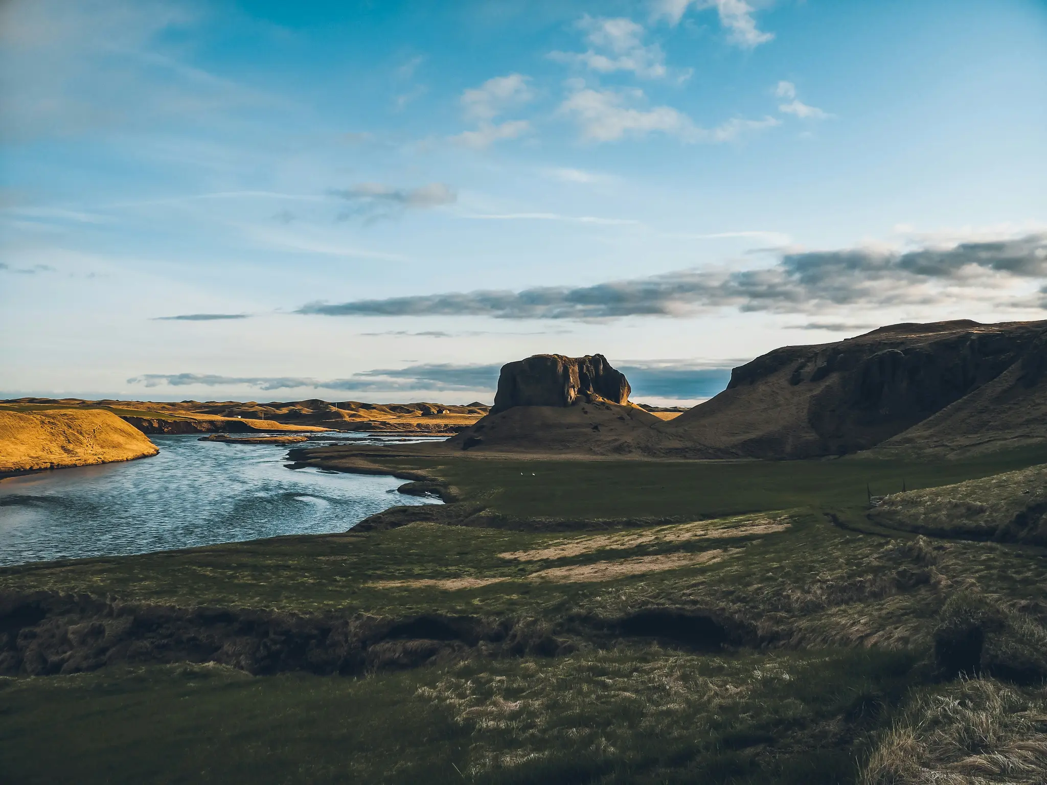 Ett brett landskapsfoto visar en flod som slingrar sig genom en dal. Gröna och gyllene kullar kantar floden. En framträdande