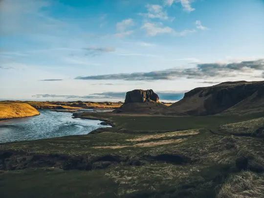 Ett brett landskapsfoto visar en flod som slingrar sig genom en dal. Gröna och gyllene kullar kantar floden. En framträdande