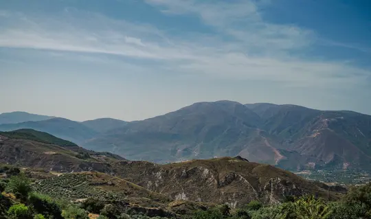 En vidvinkelbild av en bergskedja med flera lager av kullar och berg som avlägsnar sig i fjärran under en blå himmel.