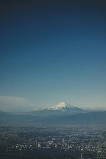 En luftvy över Fuji, dess snötäckta topp reser sig över en vidsträckt stad med många byggnader och en klarblå himmel.
