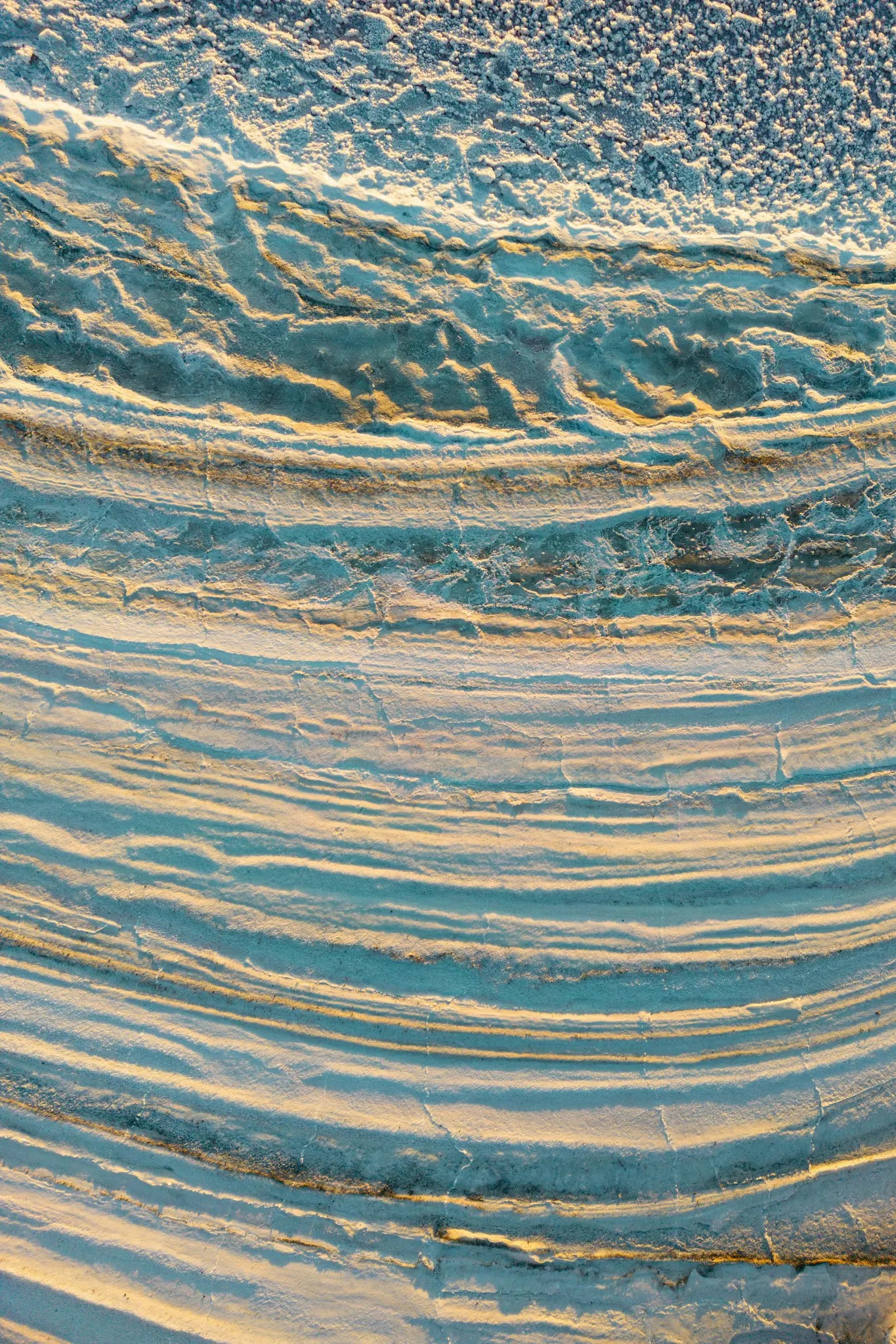 Een abstracte close-up van getextureerde, gelaagde oppervlakken. Gouden licht verlicht de richels en werpt lange