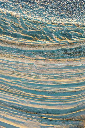Un primer plano abstracto de superficies texturizadas y en capas. La luz dorada ilumina las crestas, proyectando largas