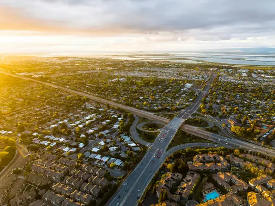 Una vista aérea de un área suburbana al atardecer, que muestra un complejo intercambiador de autopistas, casas residenciales