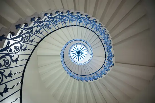O fotografie dintr-un unghi jos al unei scări elicoidale albe cu balustrade complexe din fier forjat albastru închis, care