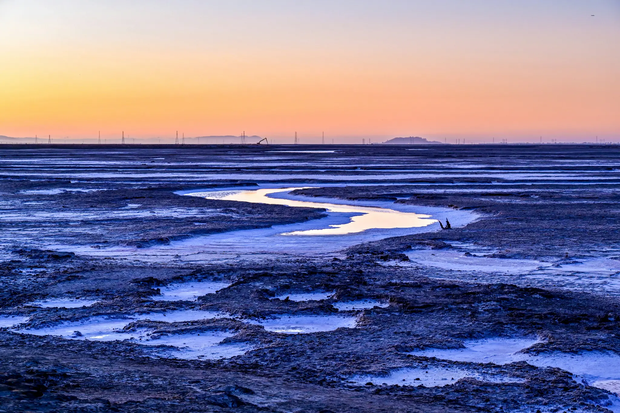 Een brede landschapsfoto van een kronkelende beek die de oranje en gele zonsondergang weerspiegelt en door donkerblauw en...