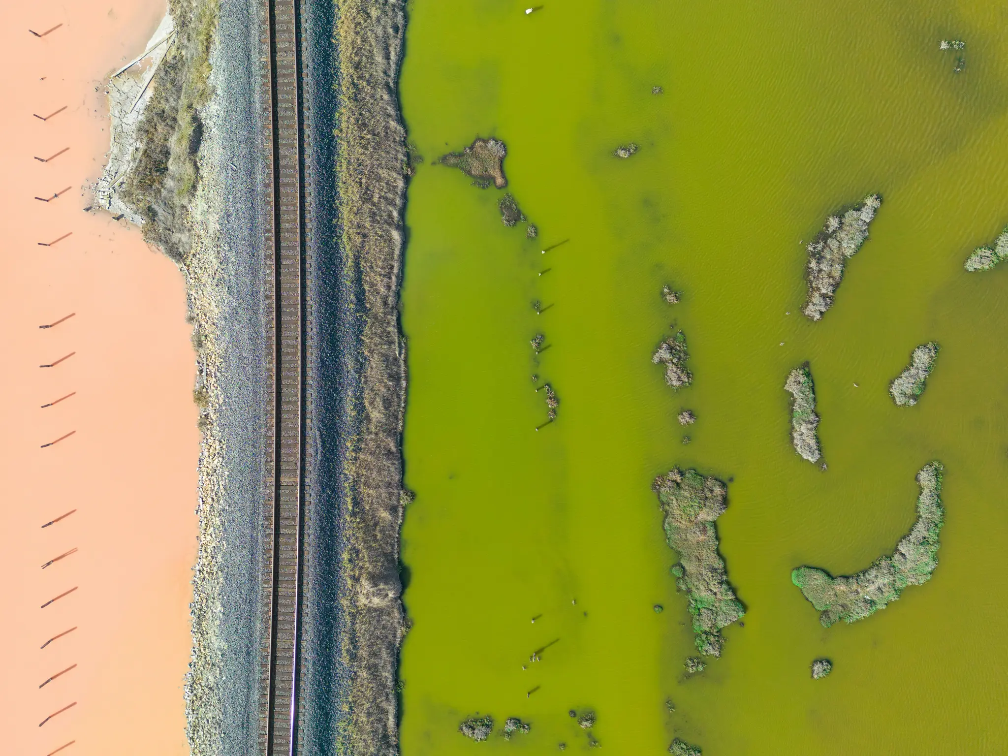 Een luchtfoto van een spoorlijn die verticaal loopt en een levendig oranje waterlichaam scheidt van een helder groen