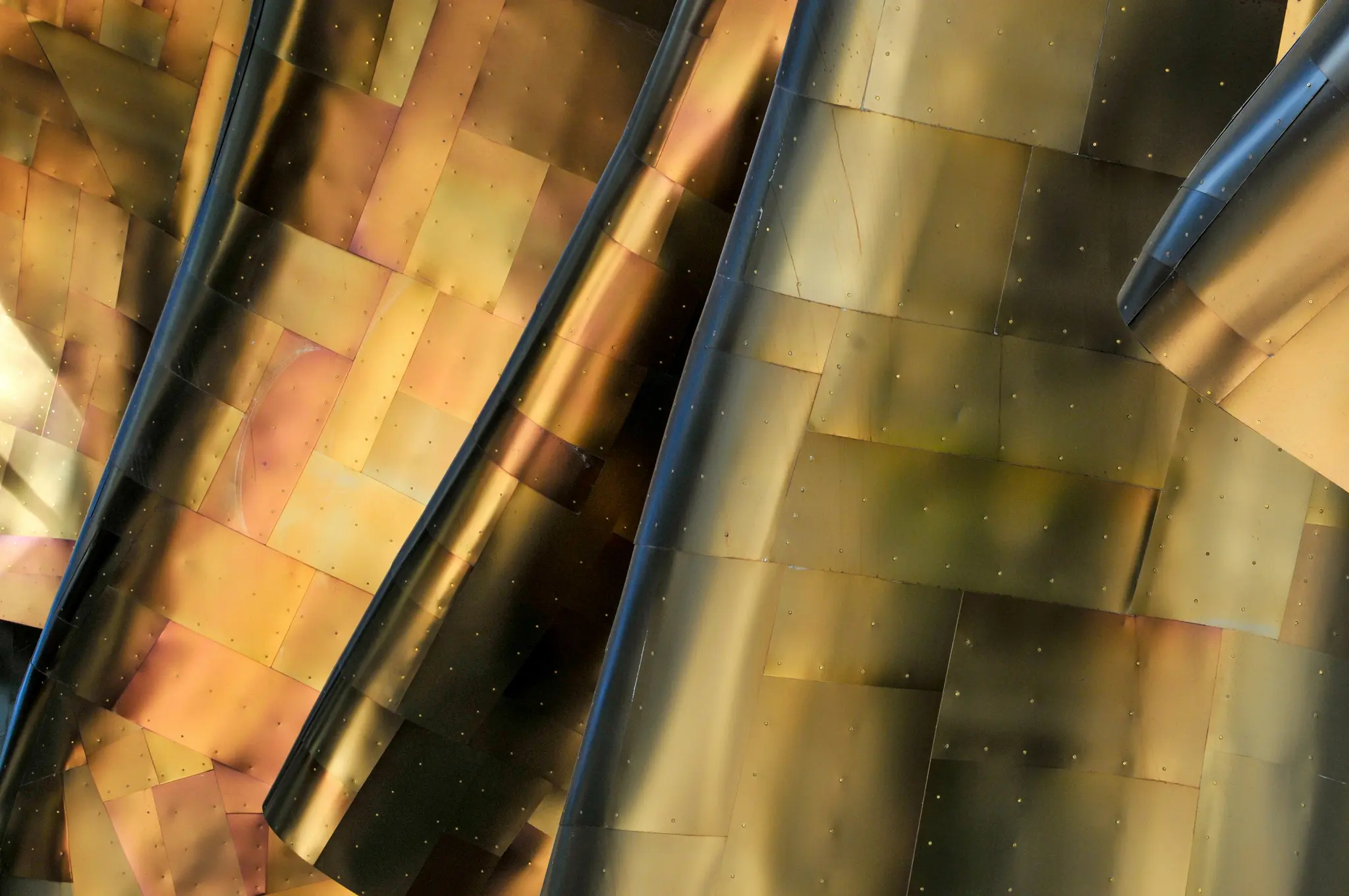 Primo piano, vista astratta dell'esterno di un edificio, con pannelli metallici curvi e sovrapposti in tonalità dorate e...