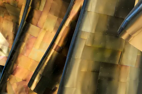 Vista cercana y abstracta del exterior de un edificio, con paneles metálicos curvos y superpuestos en tonos dorados y...
