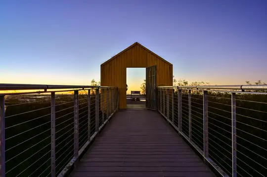 Un paseo marítimo de madera con barandillas metálicas conduce directamente a una pequeña estructura amarilla con forma de