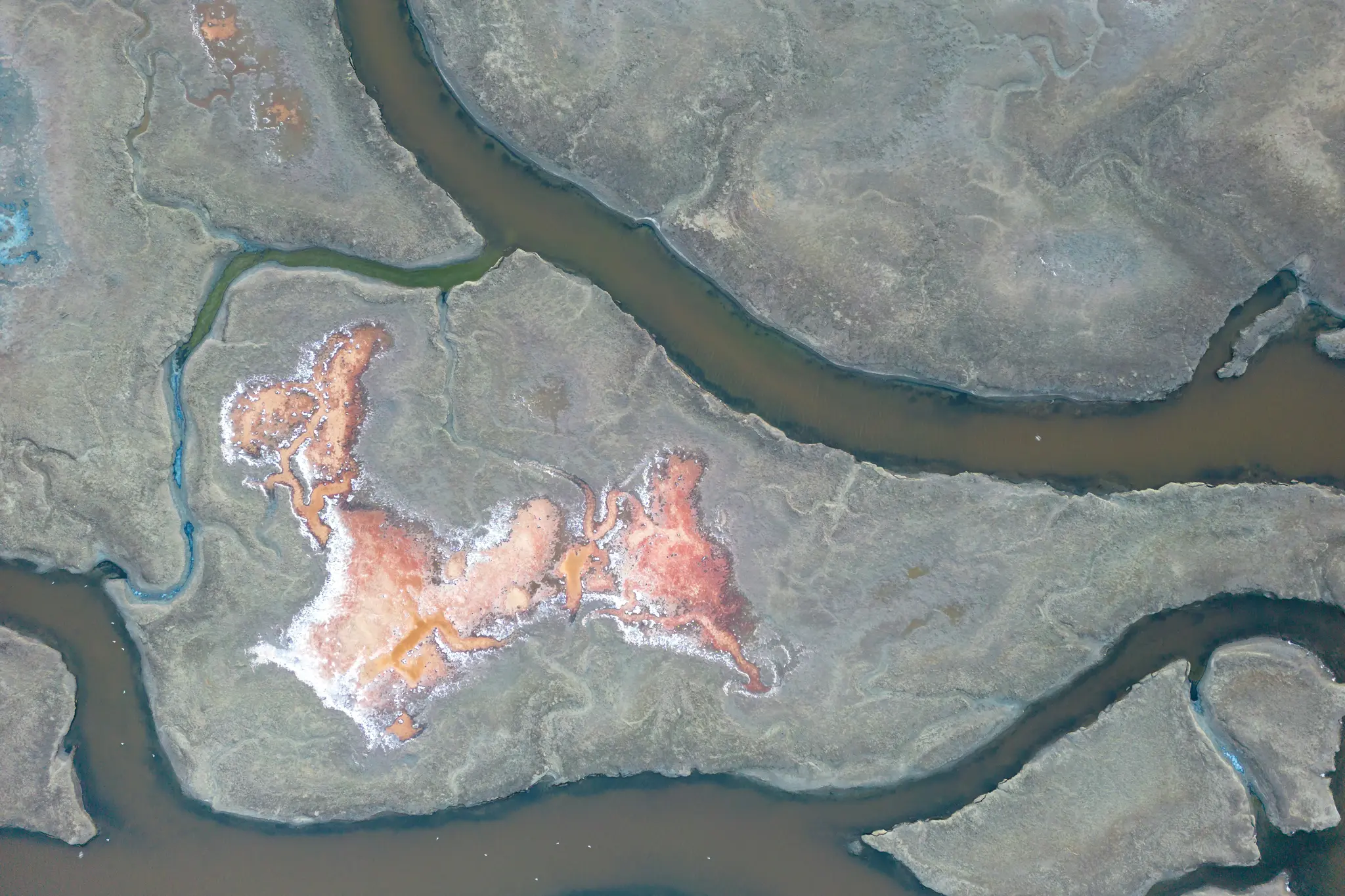 Eine Luftaufnahme zeigt einen Salzsumpf mit dunkelbraunen und grünen Wasserwegen, die sich durch graugrünes Land schlängeln.