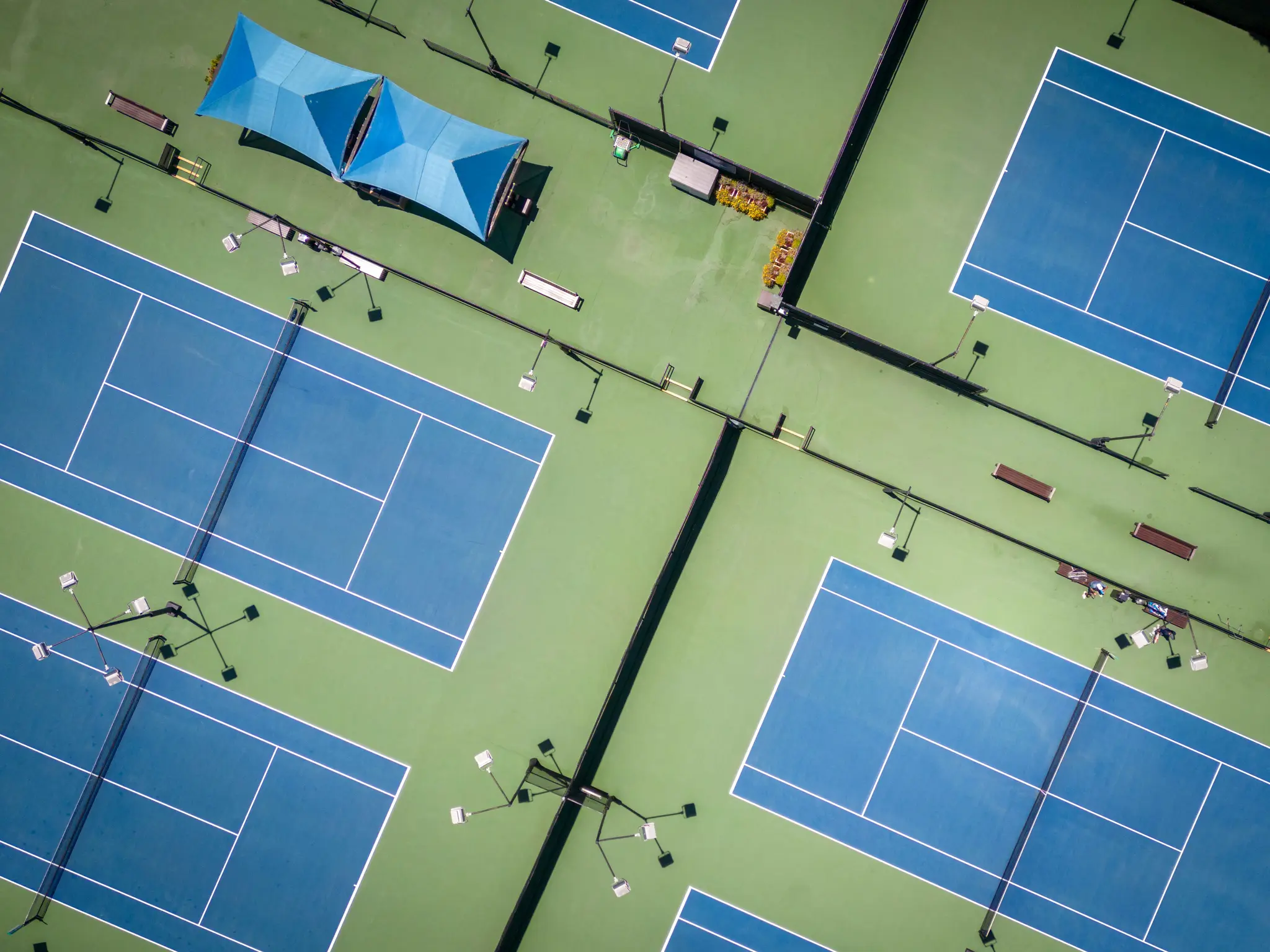 En luftvy, uppifrån, av flera blå tennisbanor med vita linjer, omgivna av grönska. Två blå skuggade områden.