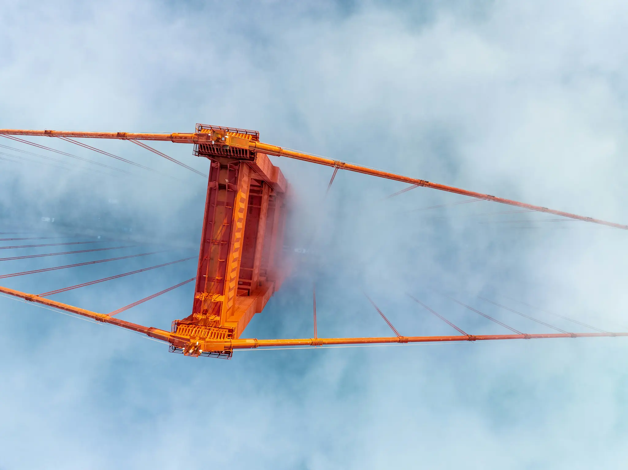 Een opwaartse opname van een oranje brugtoren, met de kabels die naar buiten uitstrekken, gedeeltelijk omhuld door witte mist