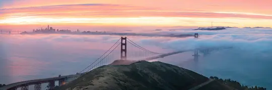 Een panoramische foto van de Golden Gate Bridge en de skyline van San Francisco bij zonsopgang, met mist die een groot deel