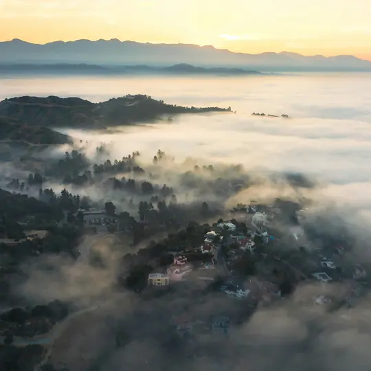 Una vista aérea muestra una zona residencial montañosa parcialmente sumergida en una espesa capa de niebla al amanecer.