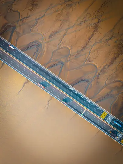 O imagine aeriană largă arată un pod de autostradă cu mai multe benzi, transportând vehicule, care se întinde pe diagonală
