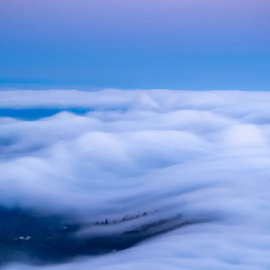Una toma de lapso de tiempo muestra una vasta extensión de nubes blancas y fluidas que cubren una cordillera, con árboles de